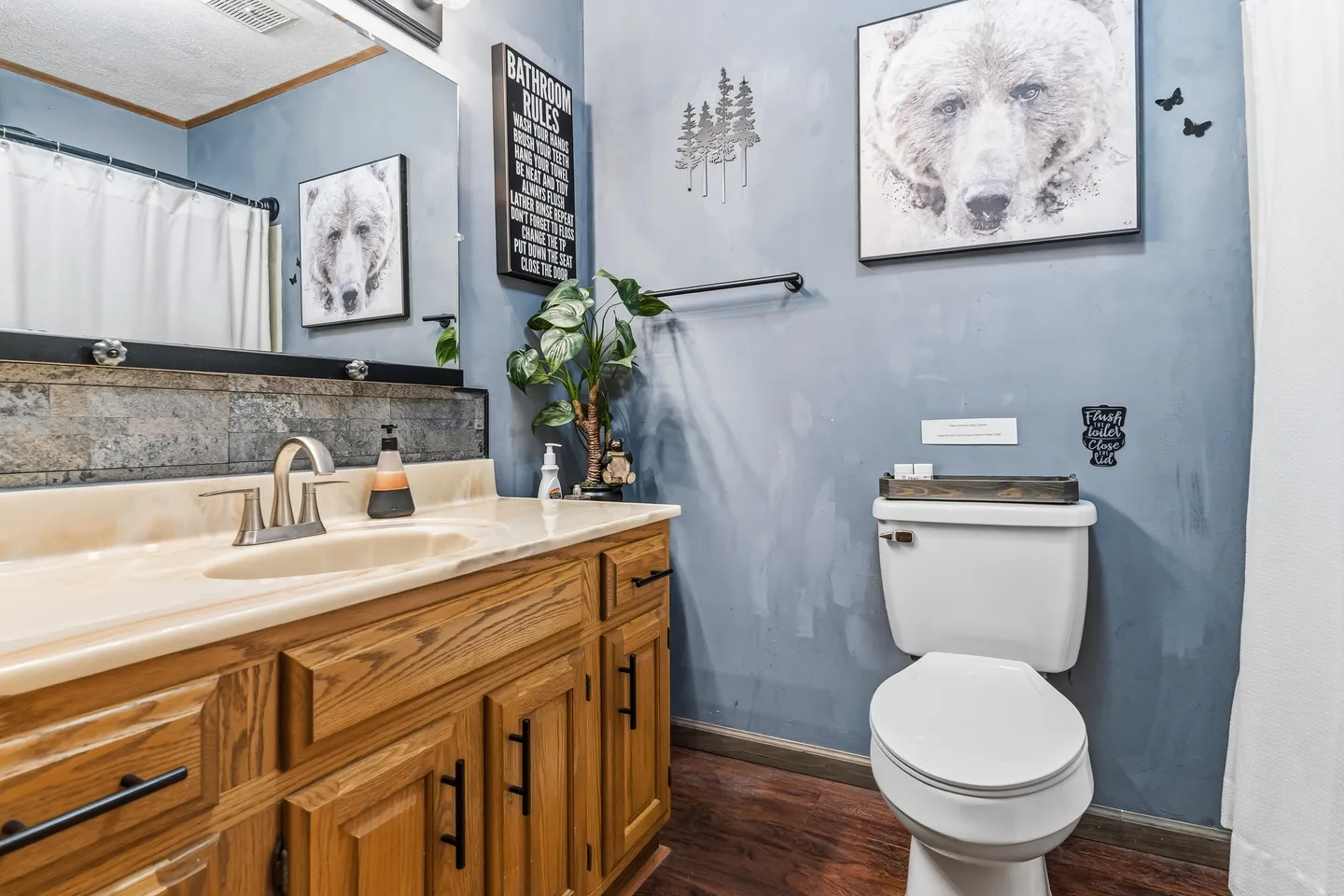 Bathroom with wooden vanity, toilet, blue walls, and bear-themed artwork.
