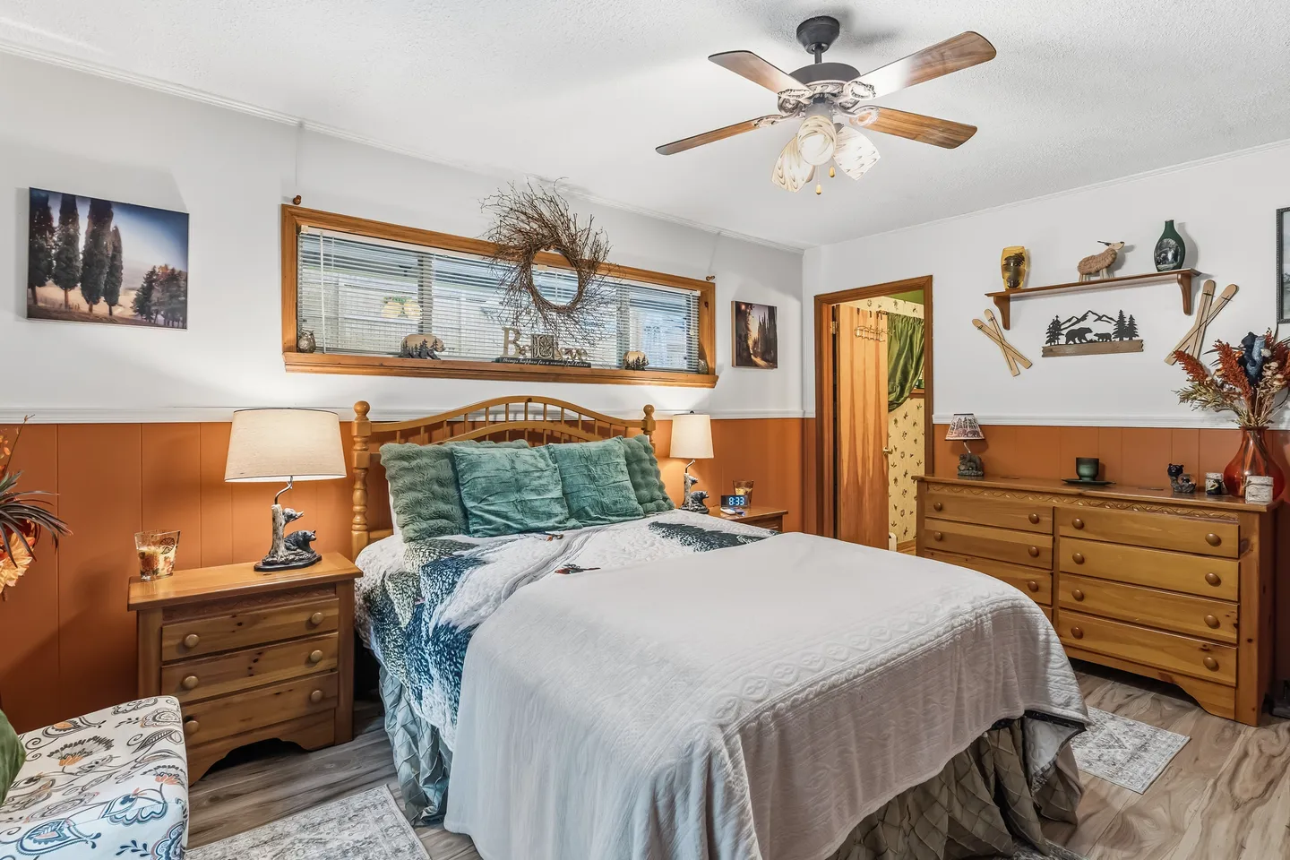 Bedroom with a made bed, wood furnishings, two-toned orange and white walls, and a ceiling fan.
