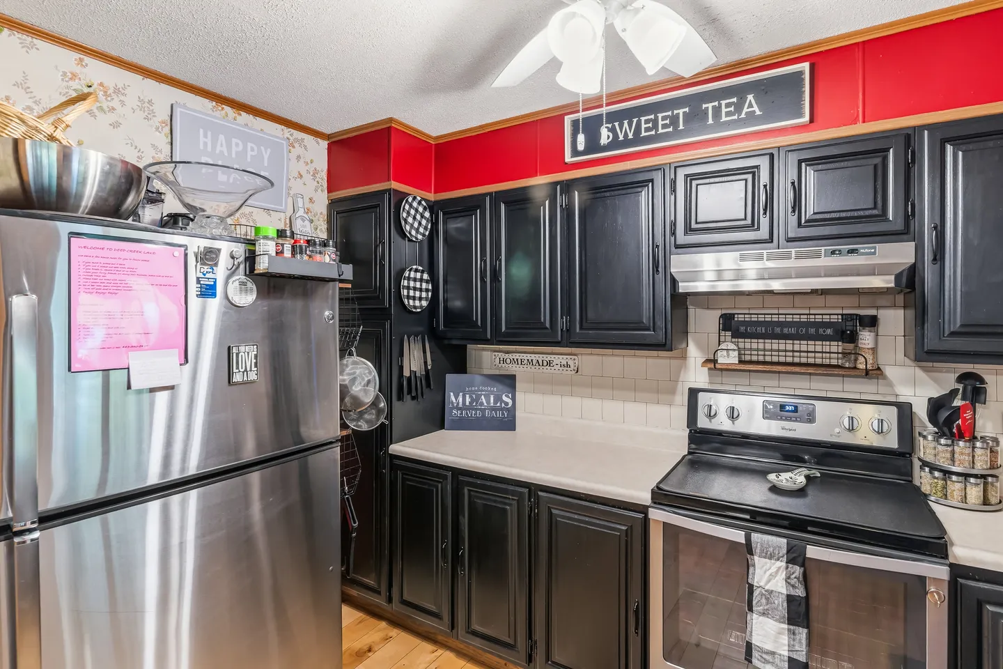 Kitchen interior featuring black cabinetry, stainless steel appliances, and a red accent border with decorative signs.