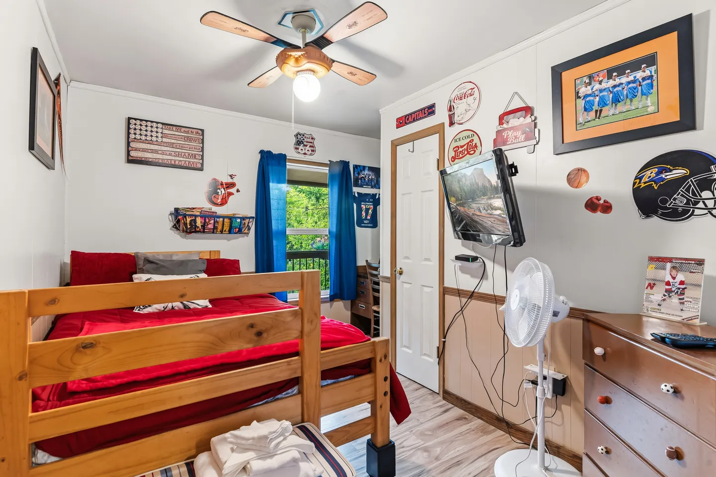 Bedroom featuring a wooden bed with red bedding, a ceiling fan, sports-themed wall decor, and a wall-mounted TV.