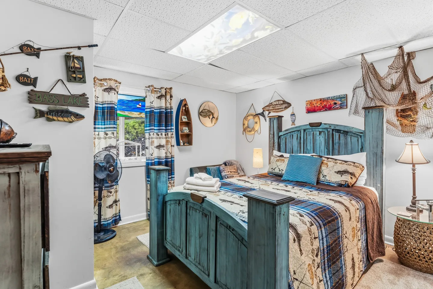 Bedroom decorated in a fishing theme with a weathered blue wooden bed, fish-patterned bedding, and fishing wall decor.