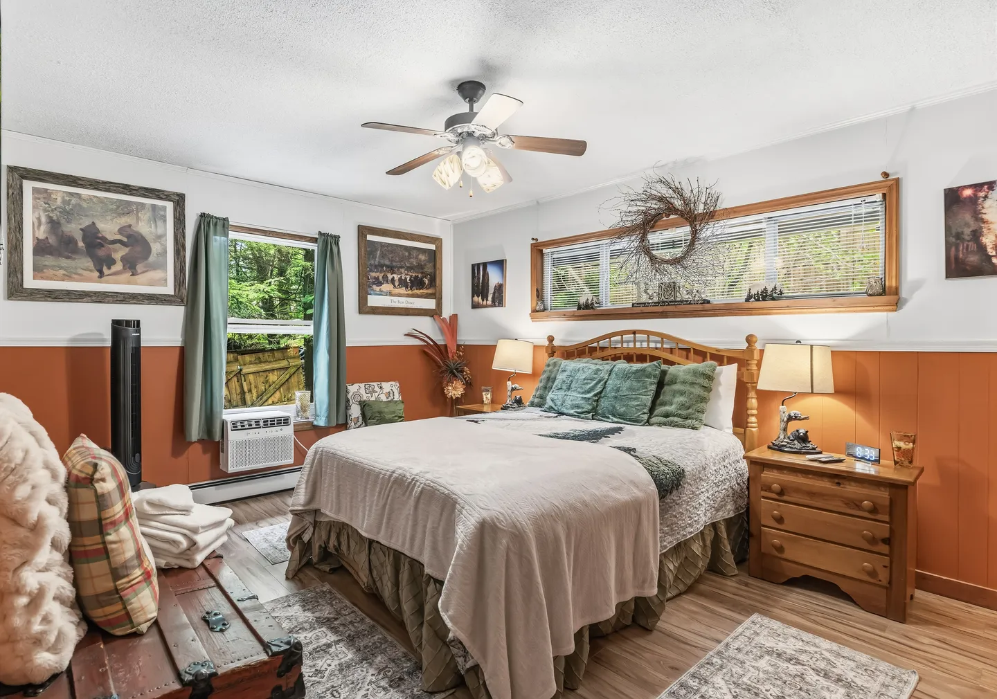 Bedroom with a wooden bed, two-tone walls, wood-look flooring, ceiling fan, and windows looking outside.