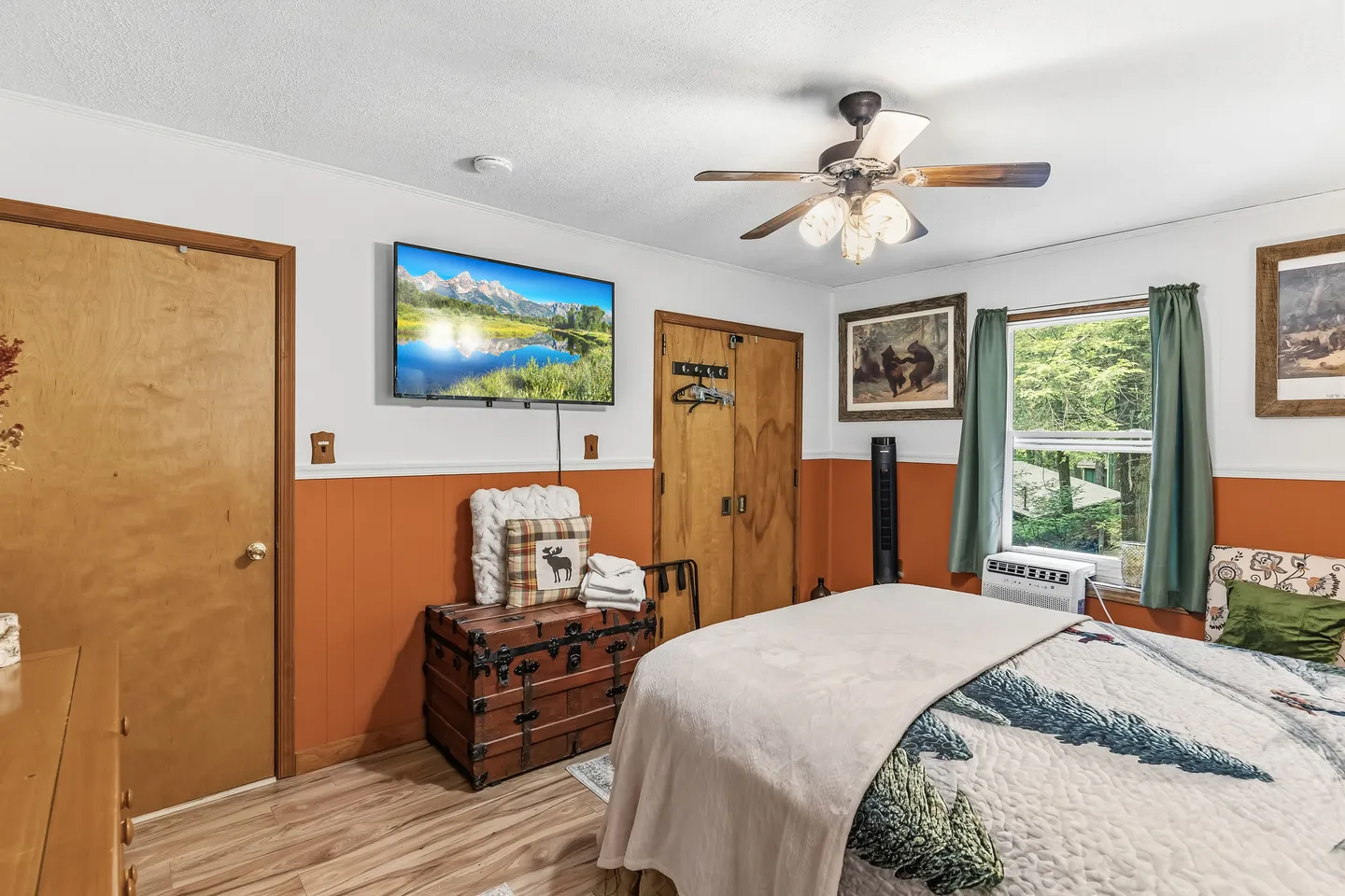Bedroom featuring a bed with nature-themed bedding, a wall-mounted TV, a ceiling fan, and two-tone white and orange walls.