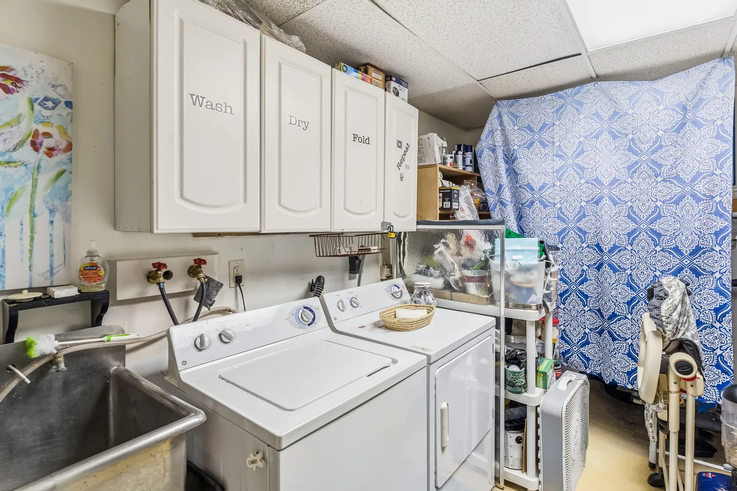 A laundry room featuring a side-by-side white washer and dryer beneath wall cabinets and next to a utility sink.