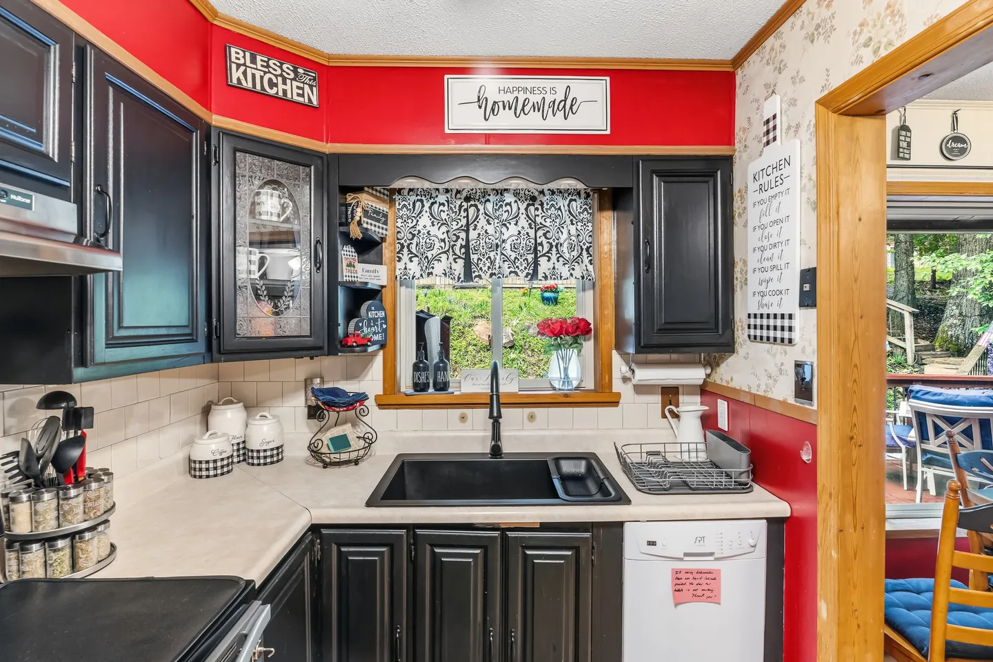 Kitchen corner showing black cabinets, a black sink, light-colored countertops, and red upper walls with decorative signs.