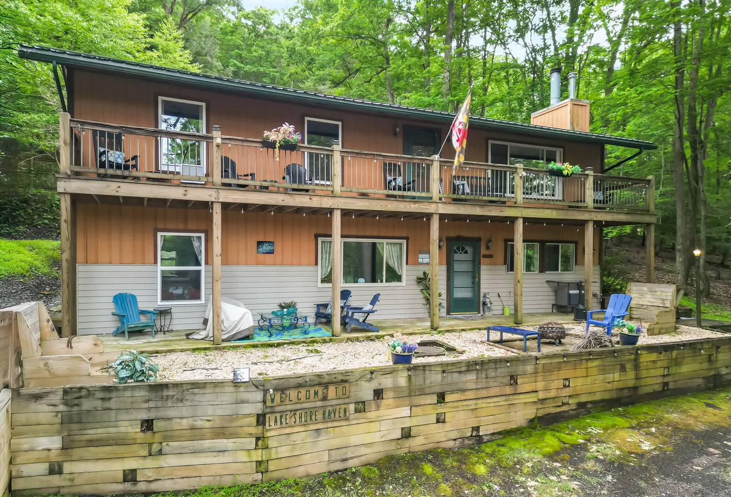 Exterior front view of a two-story home with a wide second-story wooden deck and a gravel patio area with outdoor seating.