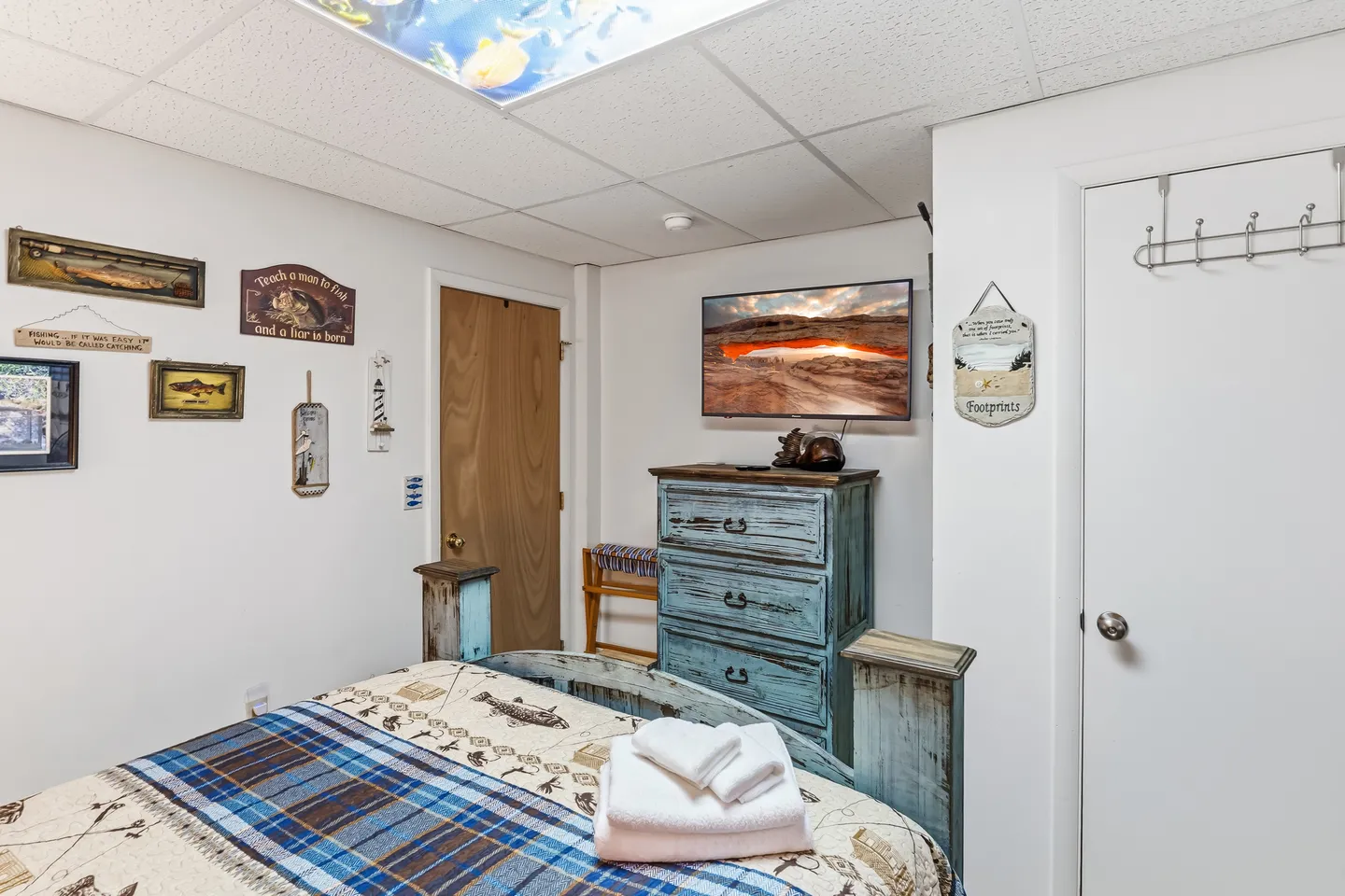 Bedroom featuring a bed with patterned bedding, a distressed blue dresser, and a wall-mounted TV.