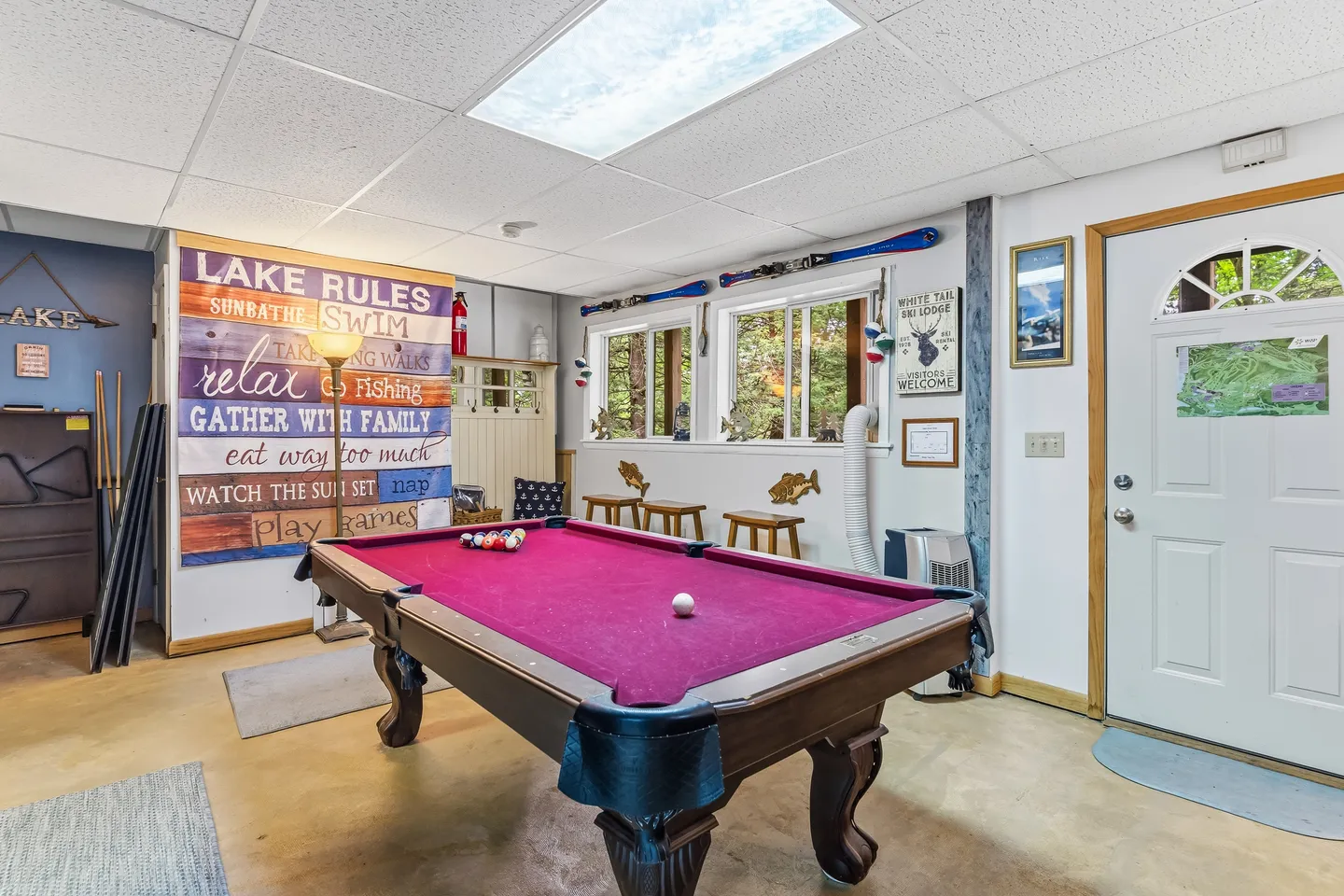 Game room featuring a wooden pool table with purple felt, wall decor, and windows overlooking greenery.