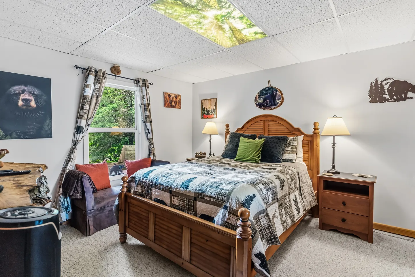 Bedroom with a wooden bed, patchwork quilt, bear-themed wall art, and an overhead light panel depicting a forest canopy.