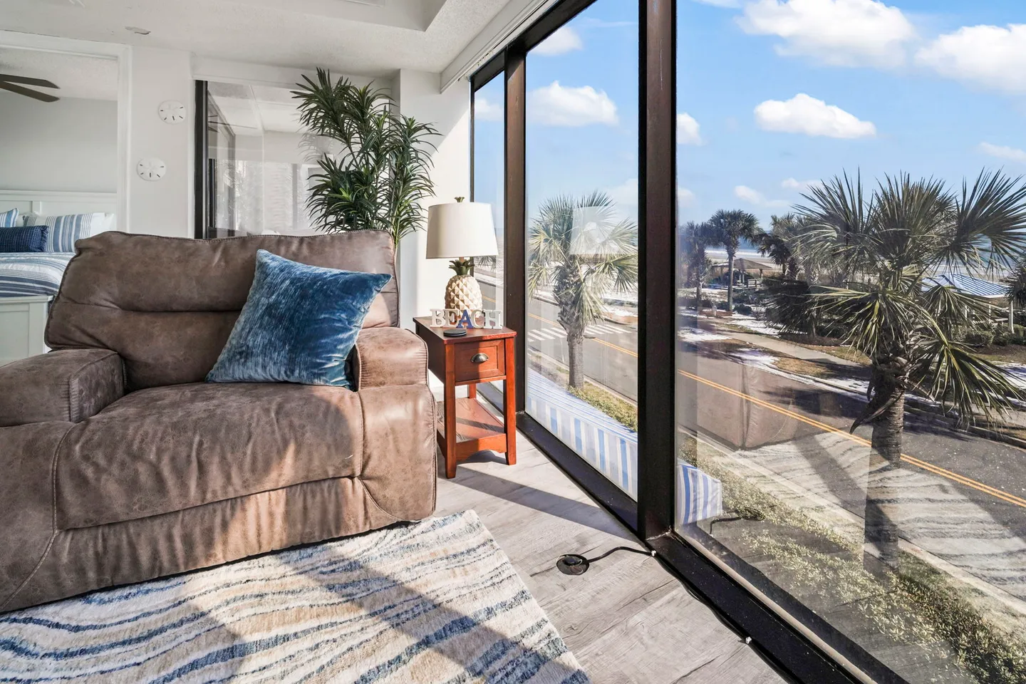 Seating area with a brown armchair beside floor-to-ceiling windows looking out onto palm trees and the ocean.