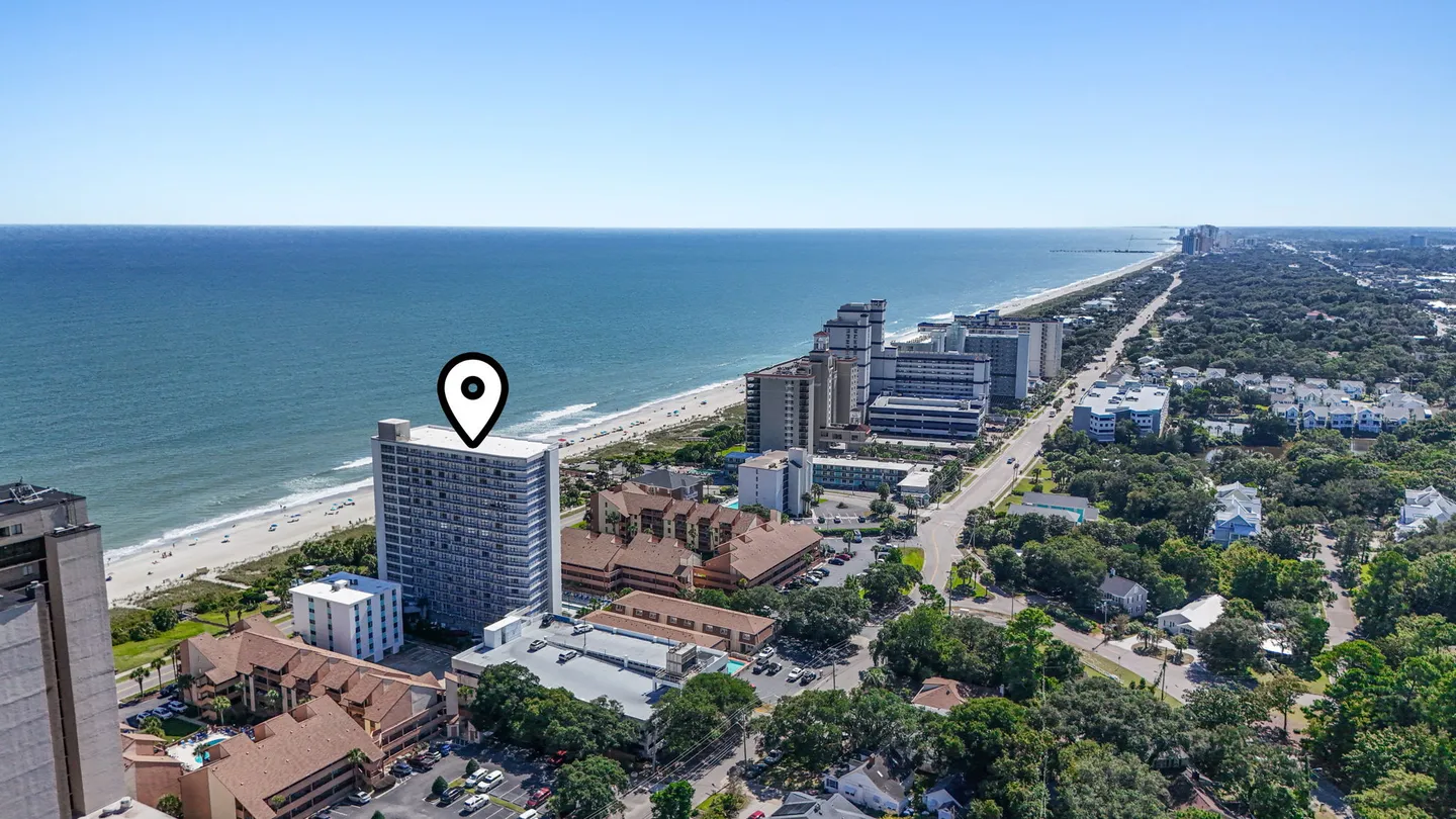 Aerial view of an oceanfront high-rise condominium building pinpointed along a sandy beach and coastline.