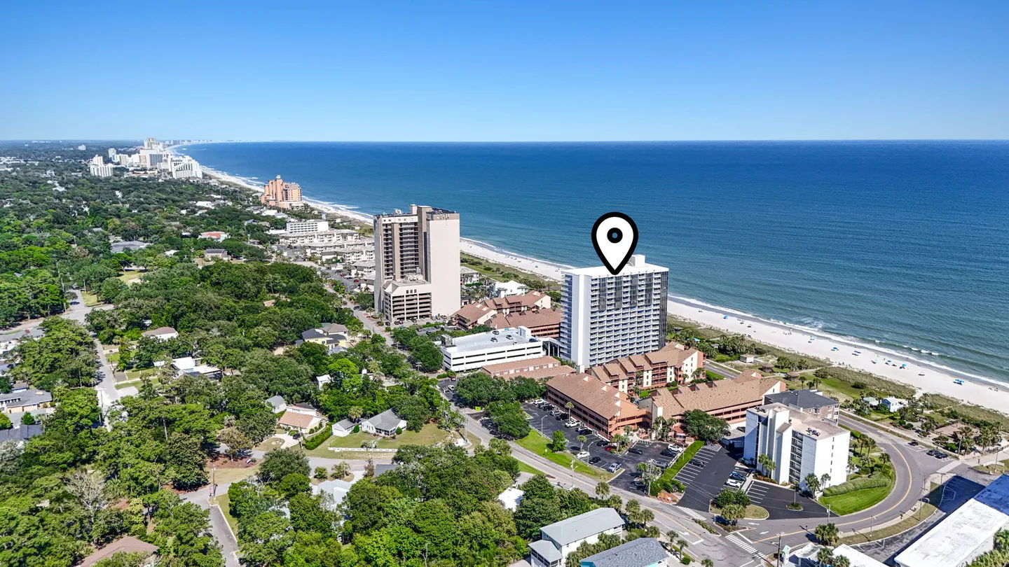 Aerial view of a coastal high-rise building marked with a location pin next to the beach and ocean.