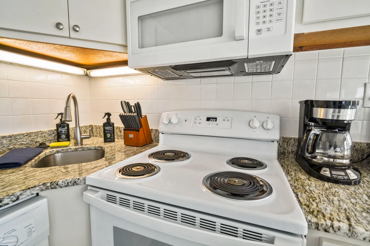 Kitchen counter area with an electric stove, over-the-range microwave, sink, and coffee maker.