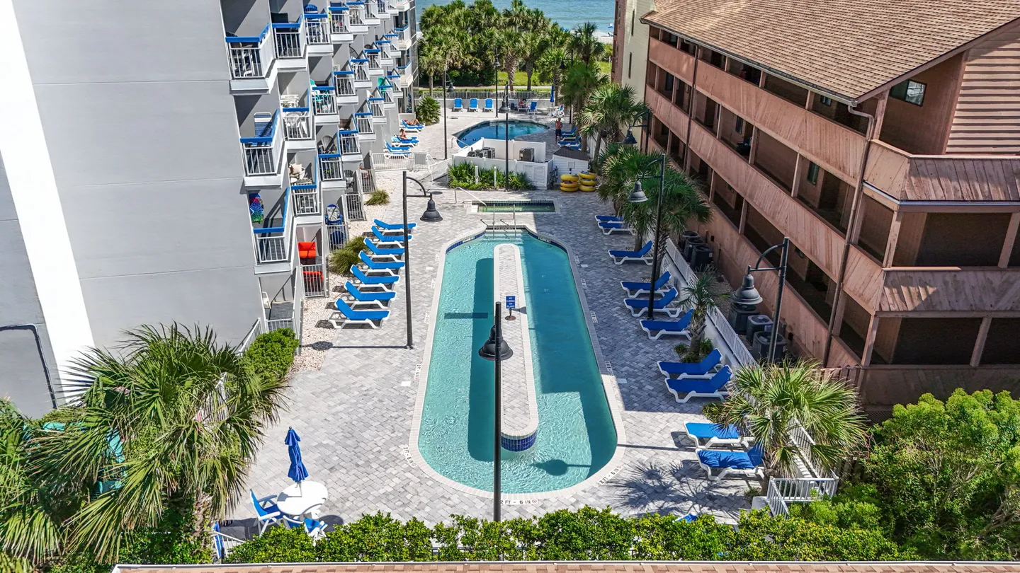 High-angle view of a resort courtyard featuring a lazy river swimming pool surrounded by blue lounge chairs and condominium buildings.