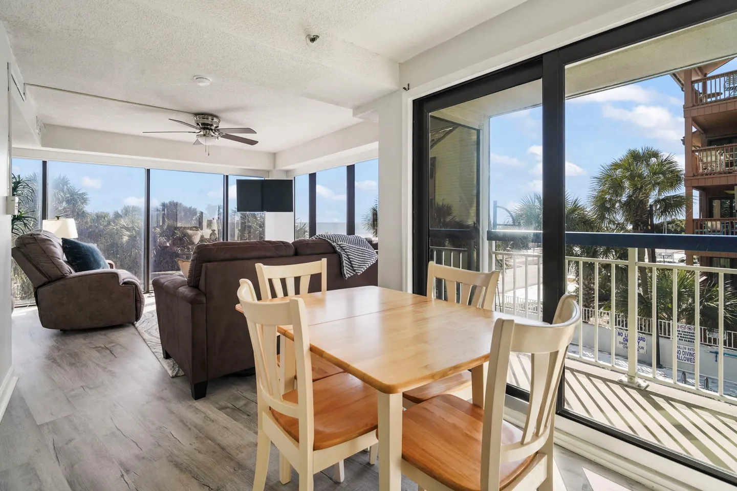 Dining table and chairs next to sliding glass doors with a view of the adjacent living area and balcony.