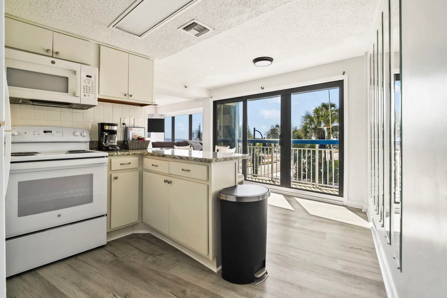 Kitchen with white appliances and light-toned cabinets next to sliding glass doors that open to a balcony.