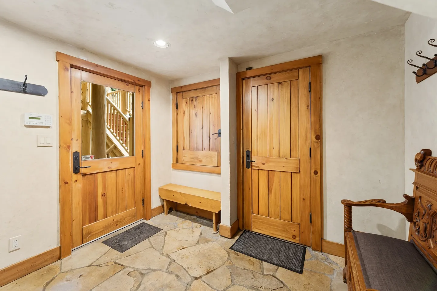 Entryway with flagstone tile flooring, wooden doors, a wooden bench, and an ornate carved bench.