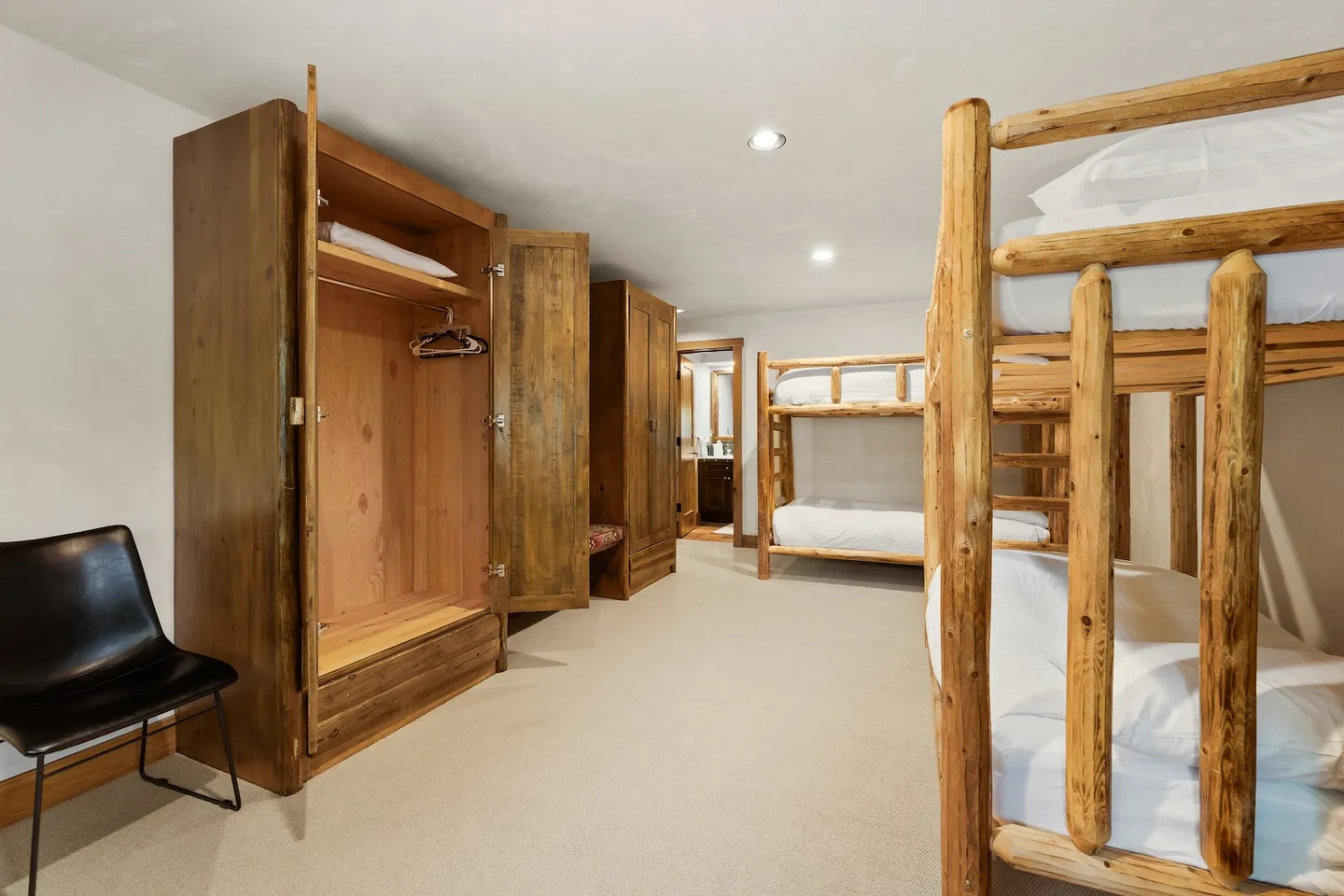 Bunk room with log-style bunk beds, carpeted flooring, large wooden wardrobe cabinets, and an open doorway leading to a bathroom.