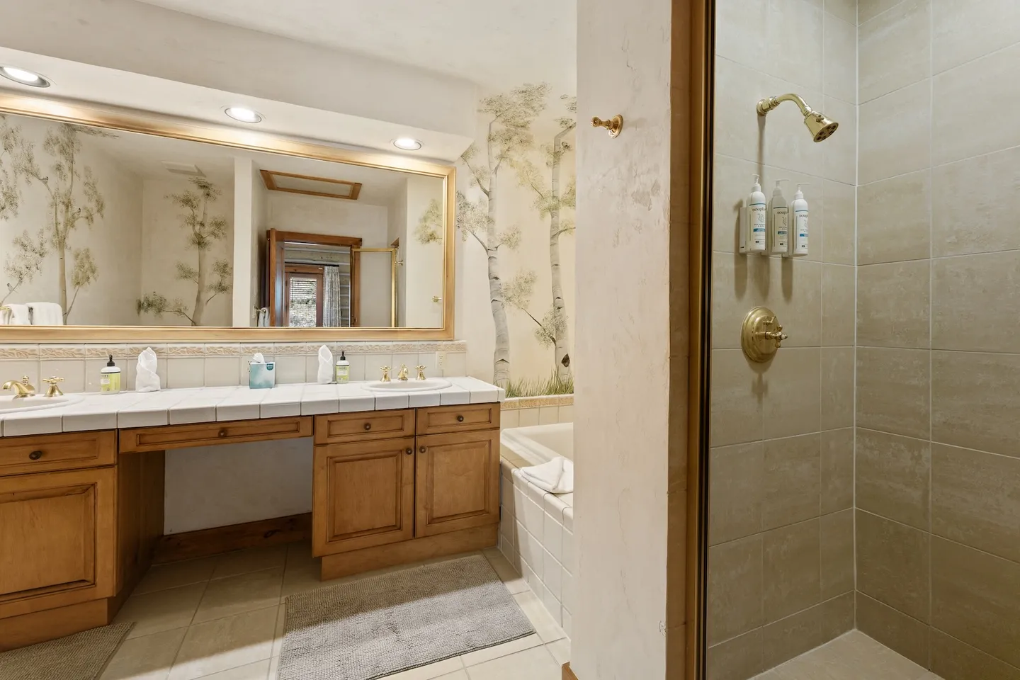 Bathroom with a double-sink vanity, large framed mirror, recessed lighting, and a walk-in shower with brass fixtures.