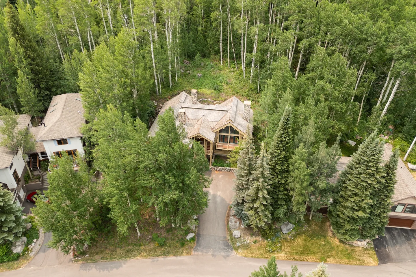 Aerial view of a multi-story home surrounded by dense green forest trees with a paved driveway.