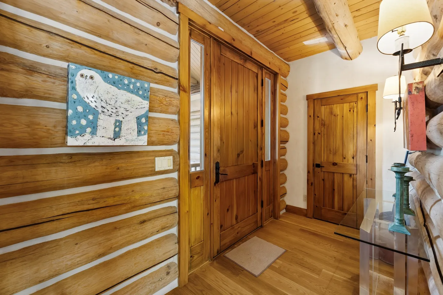 Entryway with log cabin walls, wood flooring, wooden front door with sidelight windows, and an interior wooden door.