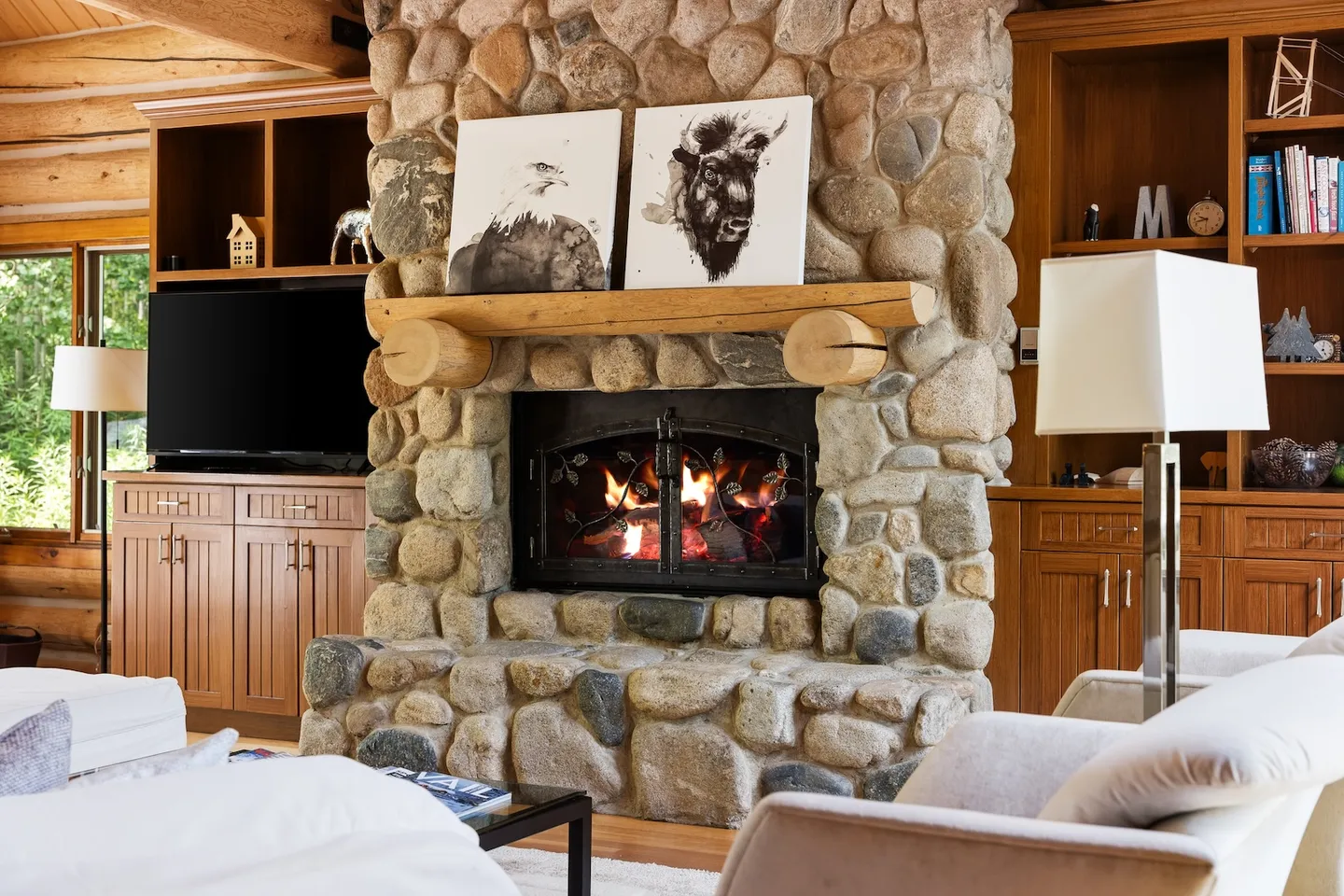 Living room featuring a central stone fireplace with a log mantel flanked by built-in wooden cabinetry and a TV.