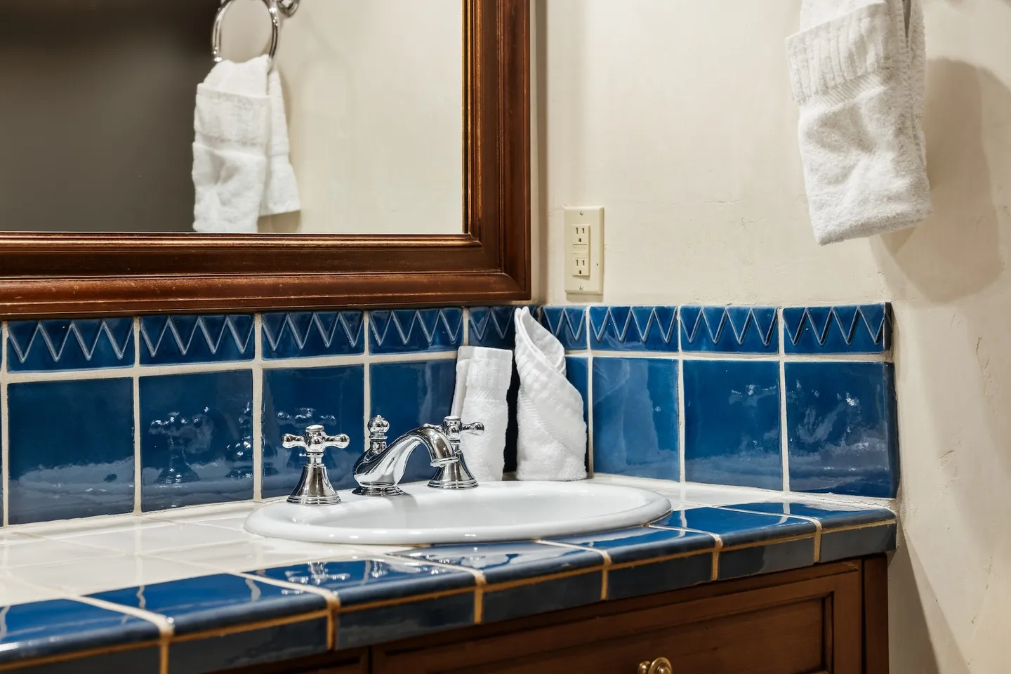 Bathroom vanity with blue tiled countertop, oval undermount sink, chrome faucet, and wooden framed mirror.