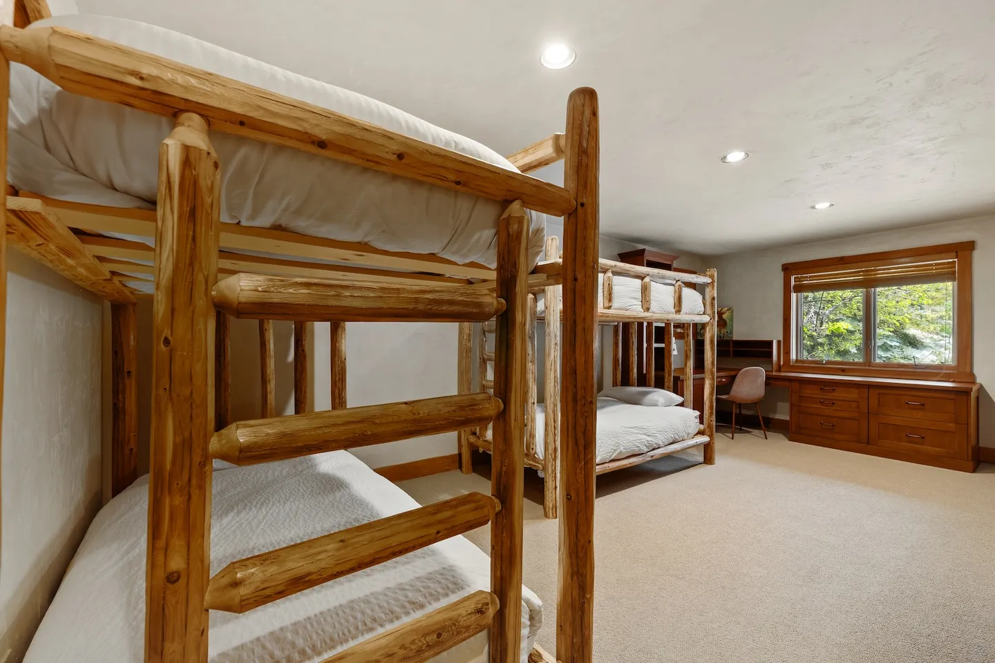 Bunk bedroom featuring log frame bunk beds, carpeted flooring, and a built-in wooden desk under a window.