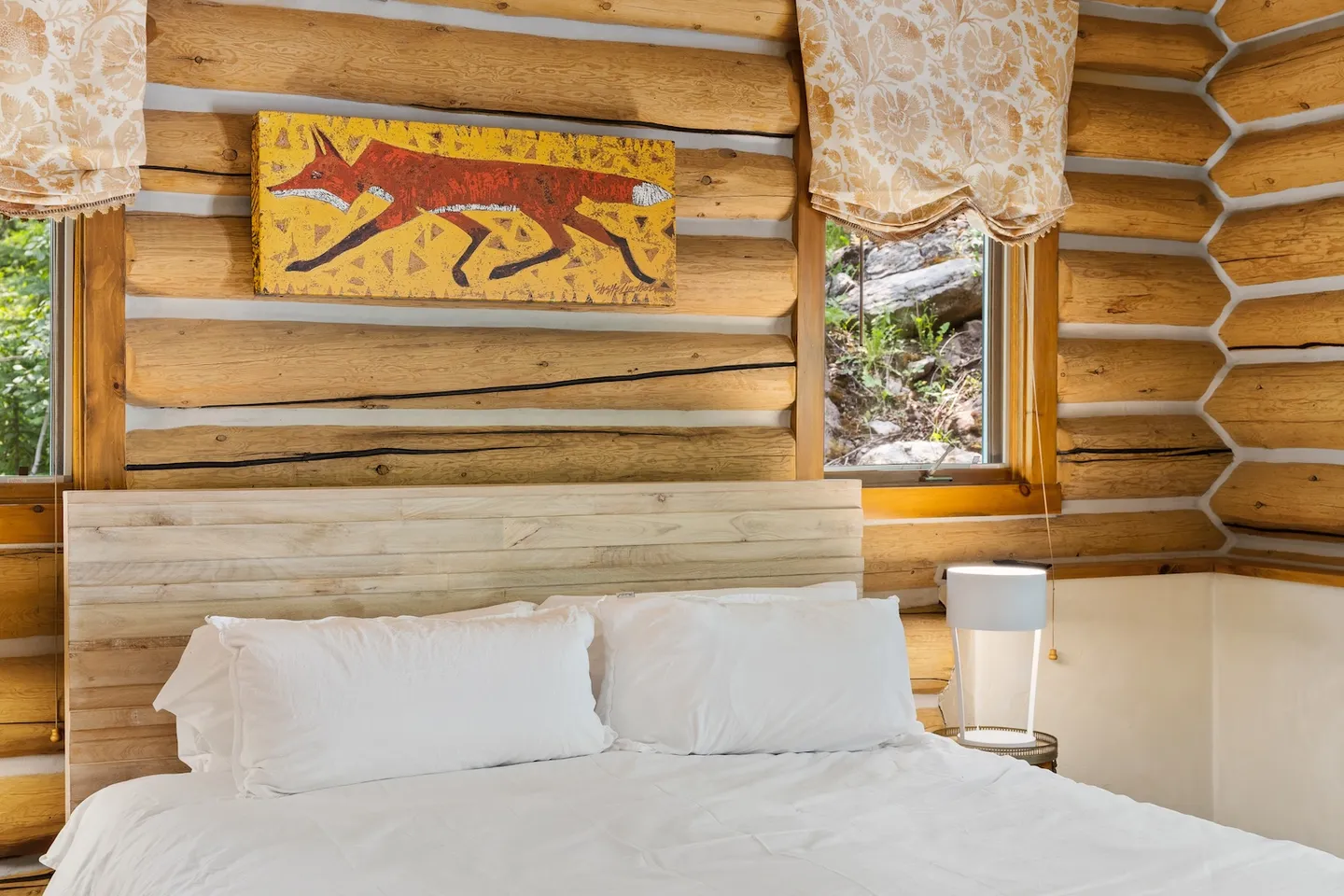 Bedroom with log cabin walls, a wooden headboard, white bedding, and fox artwork above the bed.