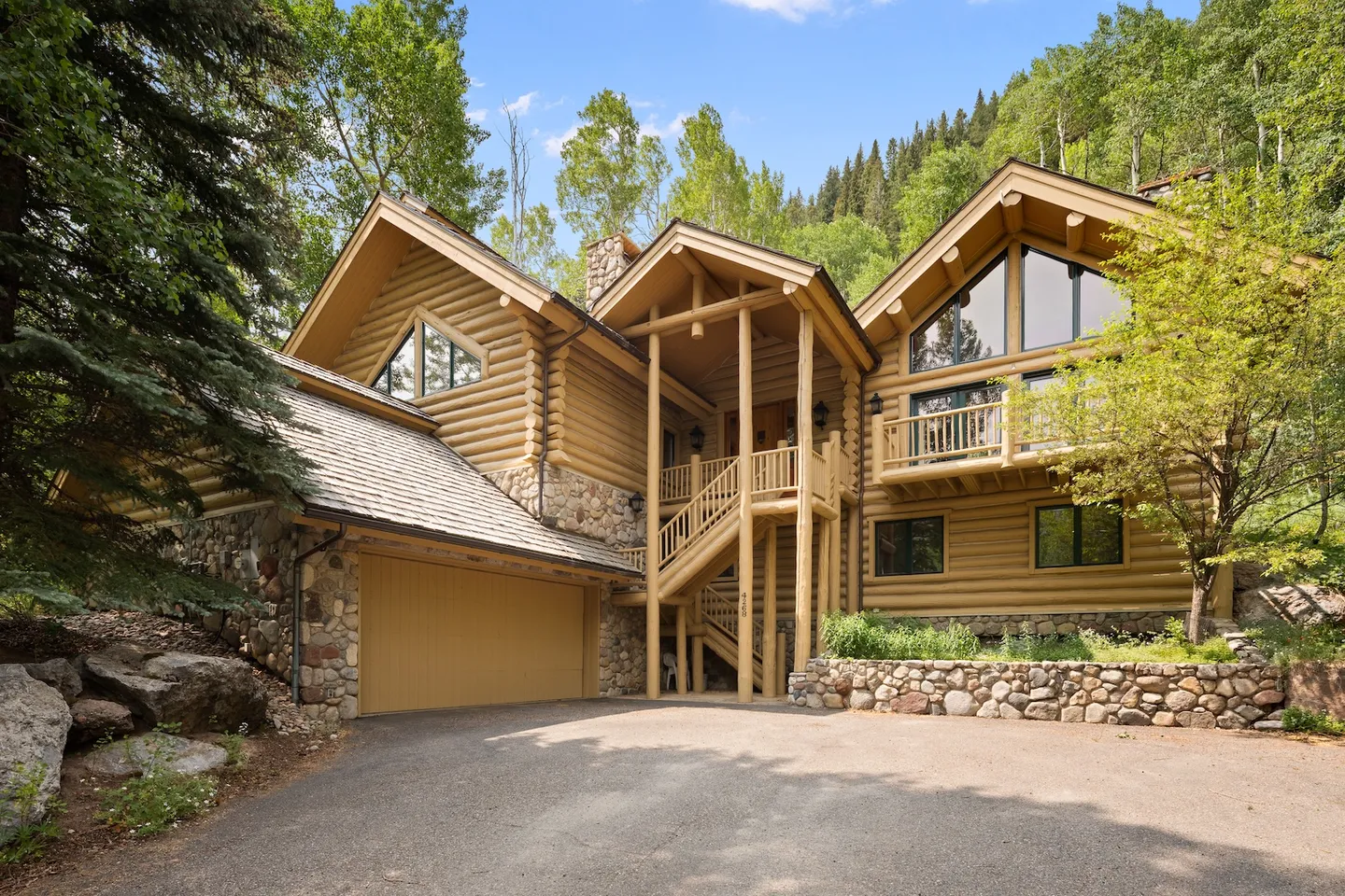 Exterior view of a multi-story log cabin home with stone accents, a paved driveway, and a garage.