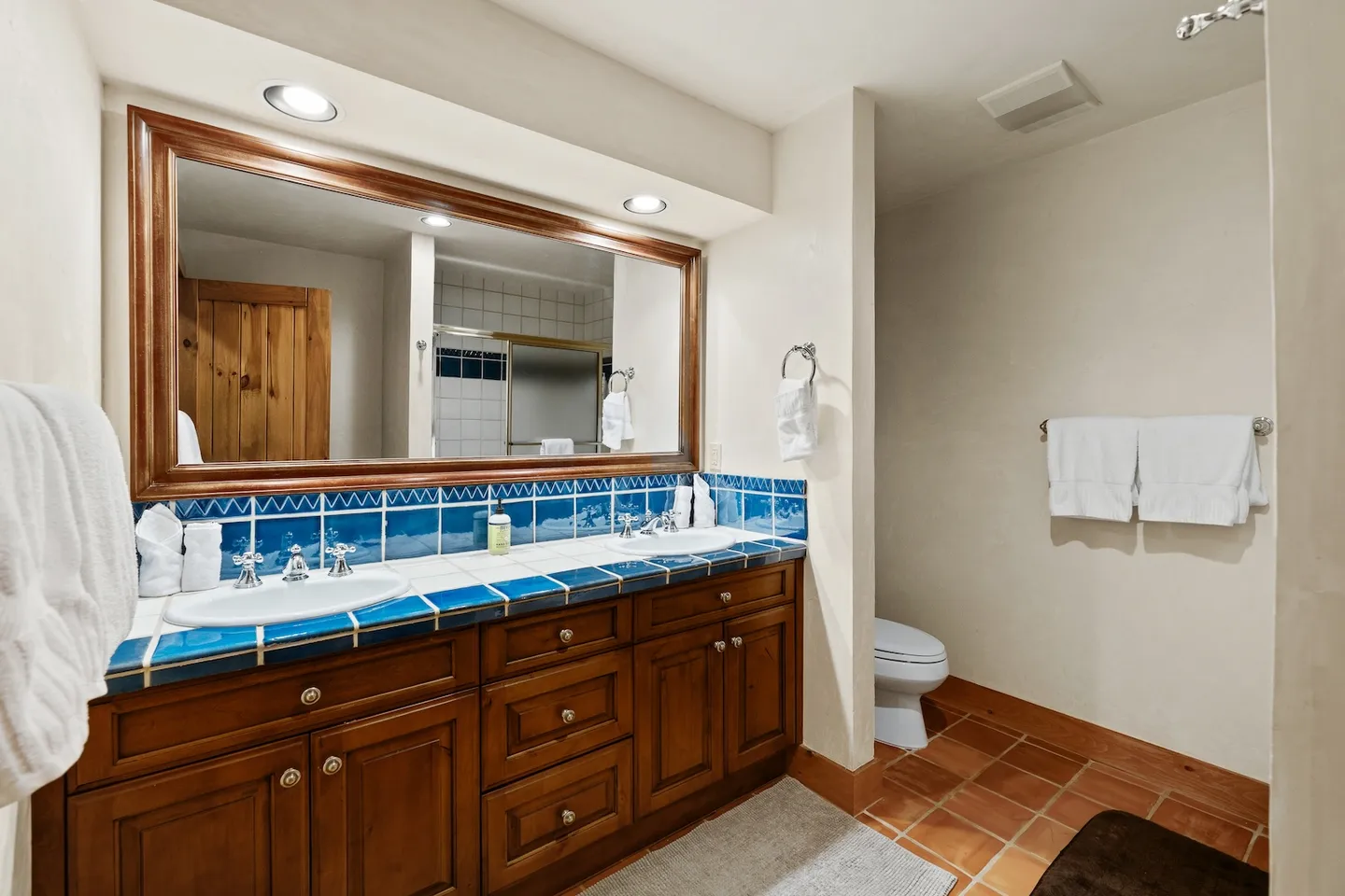 Bathroom featuring a double vanity with wooden cabinets, blue tiled countertop, a large mirror, and tiled floor.