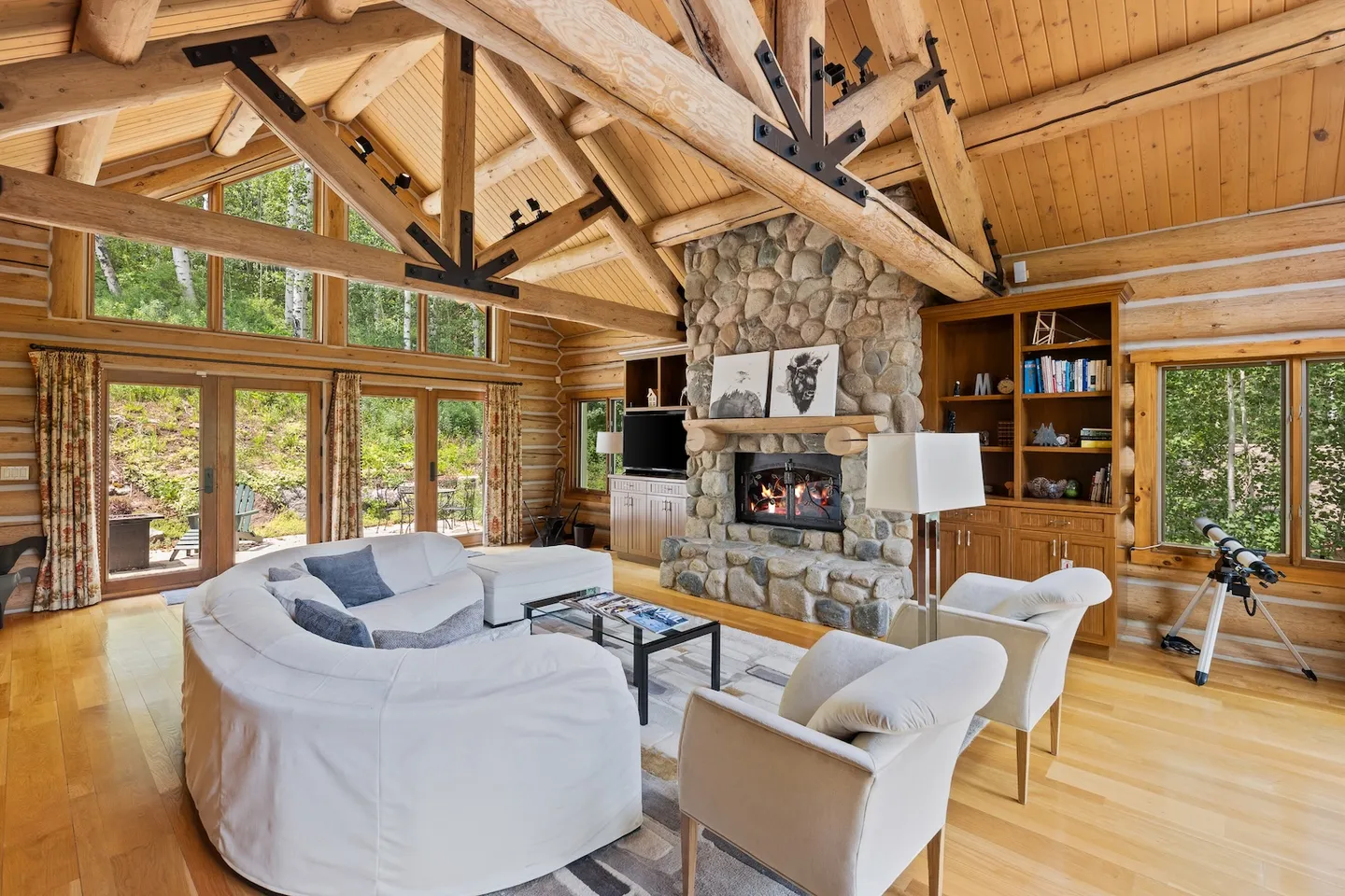 Living room with log beam vaulted ceilings, stone fireplace, and curved white sofa.