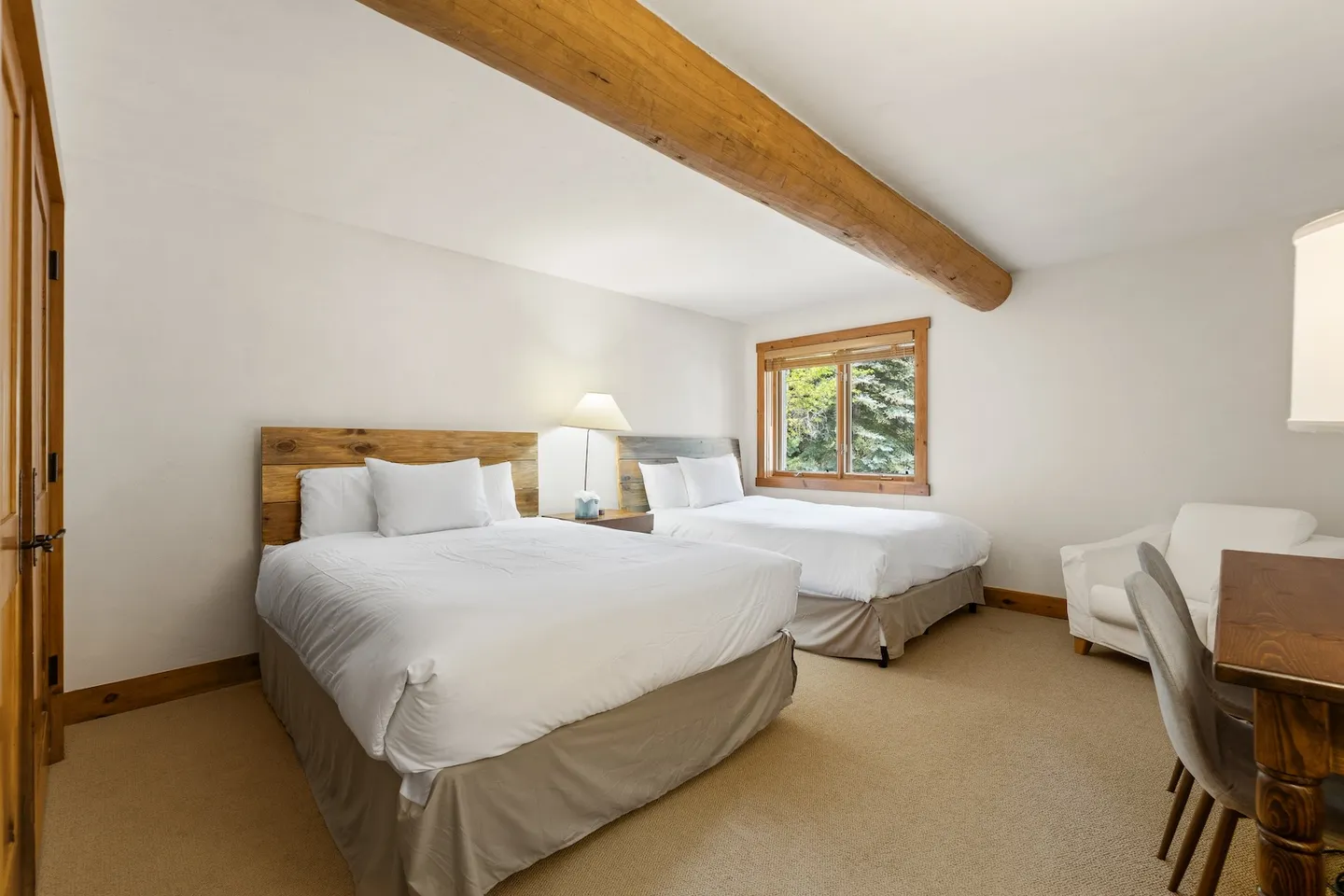 Bedroom with two beds, wood headboards, a log ceiling beam, carpeted floor, and a window.