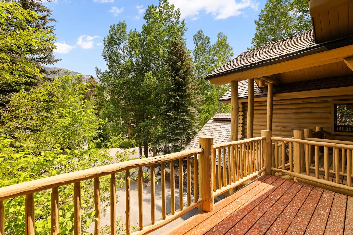 Elevated wooden deck with log railings overlooking tall green trees under a bright blue sky.