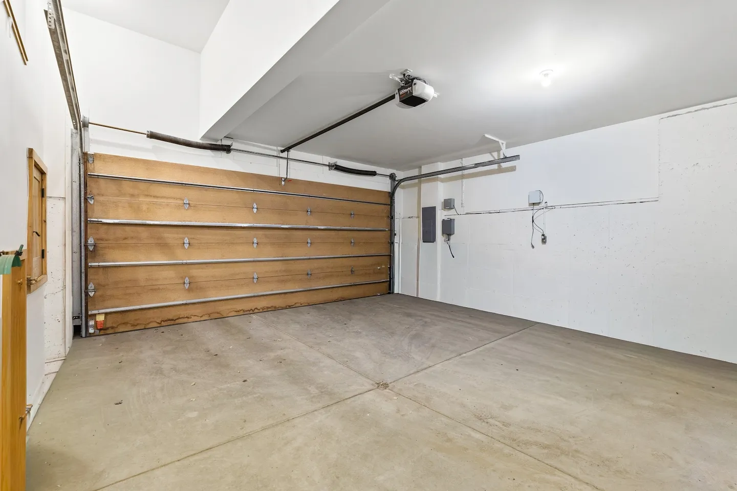 Interior view of an empty garage featuring a concrete floor, white walls, and a closed wood-paneled roll-up garage door.
