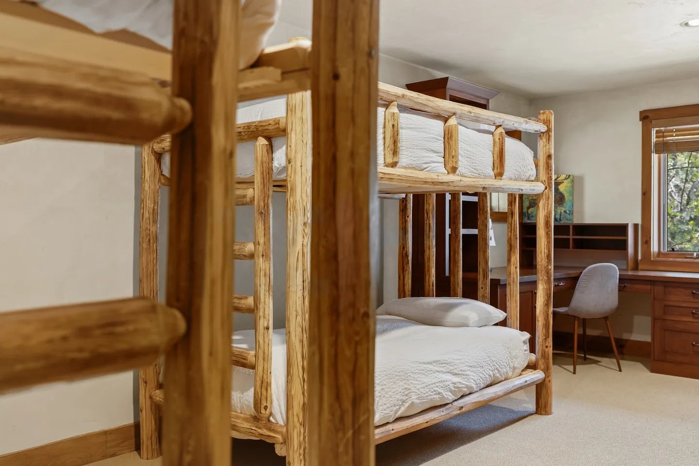 Bedroom featuring rustic log bunk beds and a built-in wooden desk with a chair.