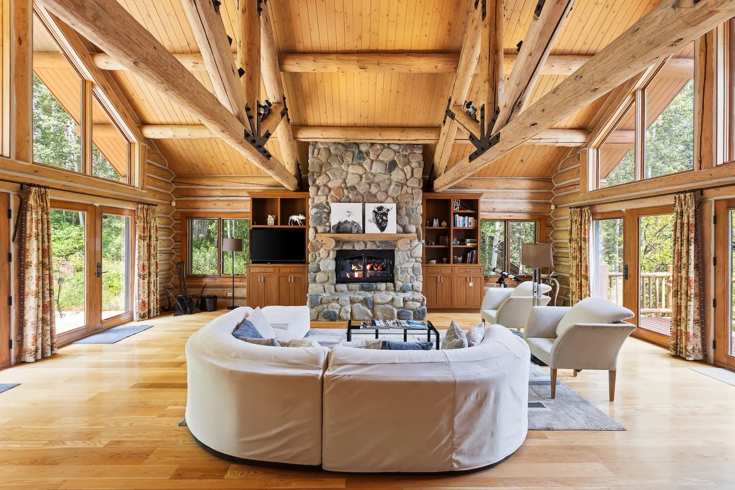 Spacious log cabin living room with a vaulted wood ceiling, stone fireplace, and curved sectional sofa.