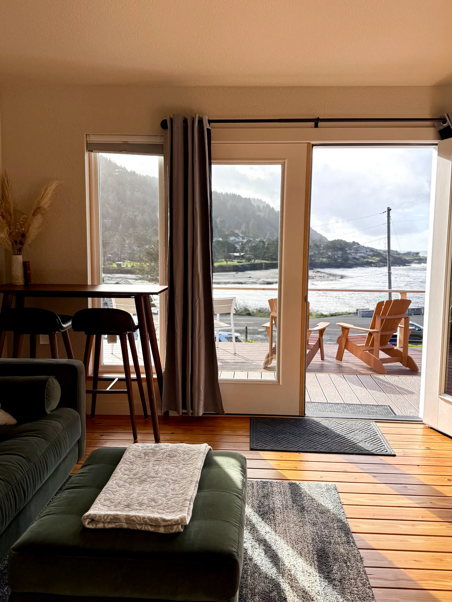 Living area with wood floors opening onto an outdoor deck with wooden chairs overlooking the ocean.
