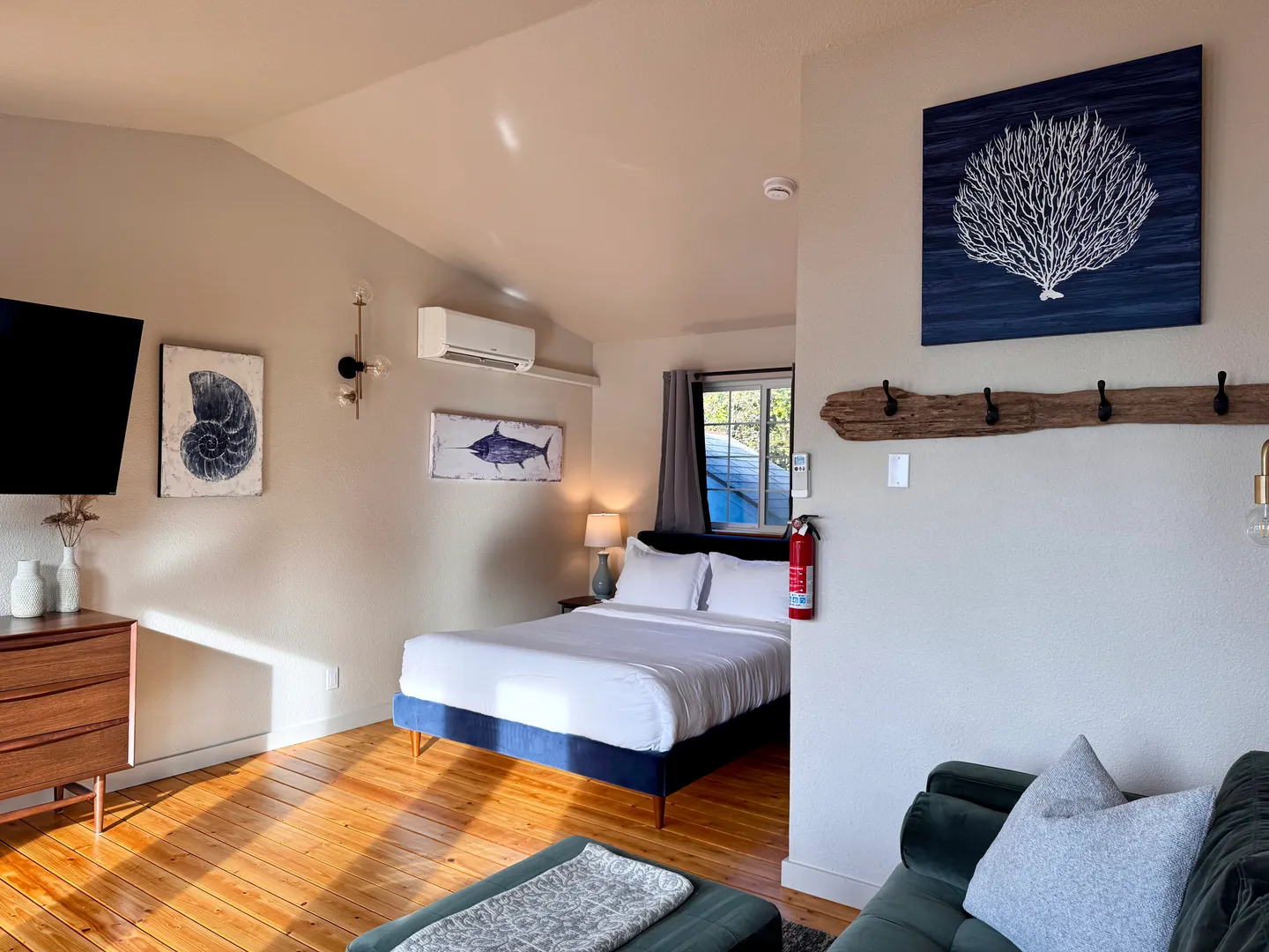 Bedroom with vaulted ceiling, wood-look flooring, a bed with a blue base, a wall-mounted TV, and coastal-themed wall art.