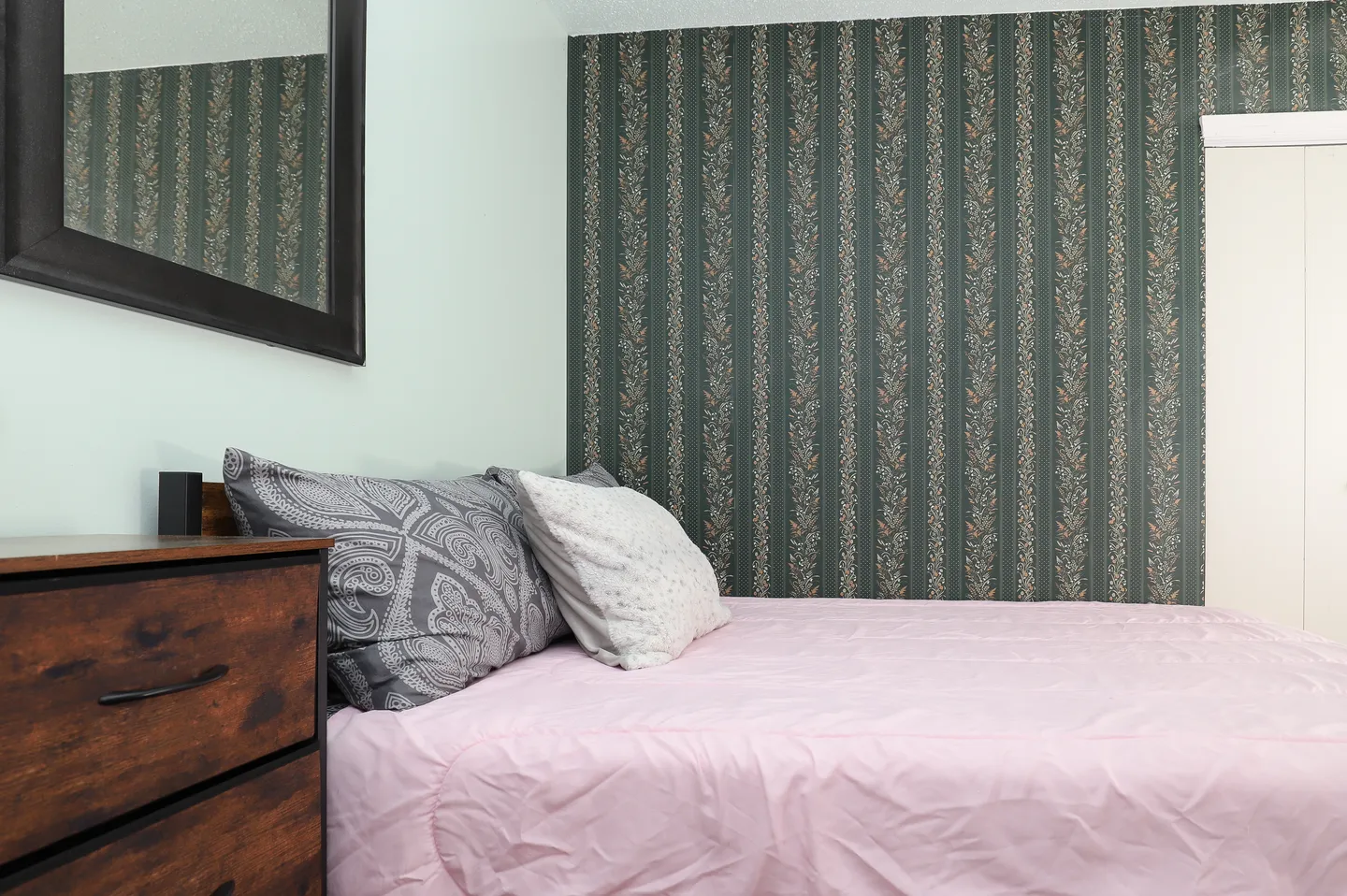 Bedroom featuring a bed with pink bedding and patterned pillows against a dark striped wallpaper accent wall.