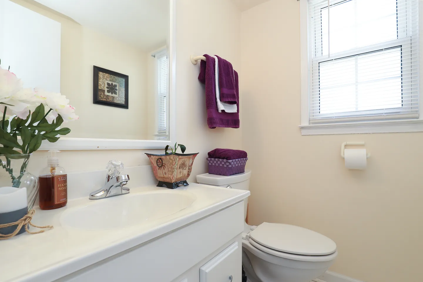Bathroom with white vanity, mirror, toilet, and a window with blinds
