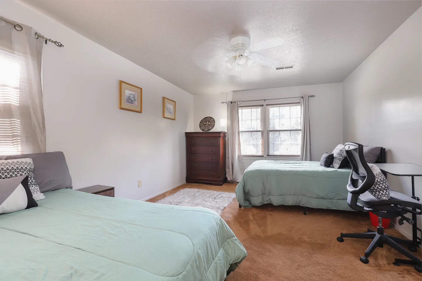 Bedroom with two beds, carpeted floor, white walls, and a small desk with an office chair.