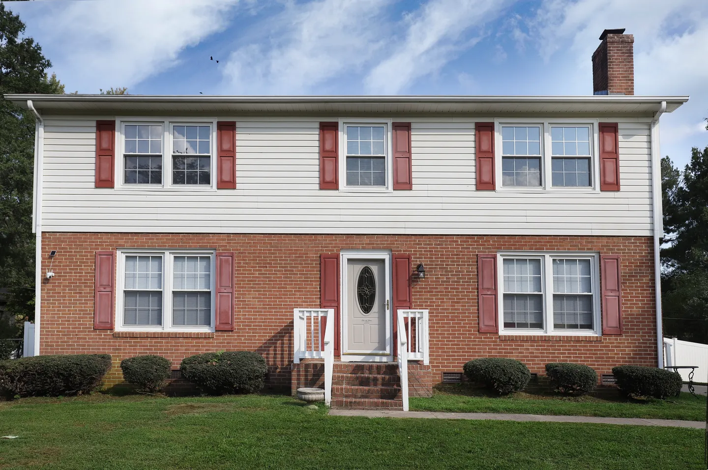 Exterior view of a two-story home featuring red brick on the first level, white siding on the second, and red shutters on the windows.