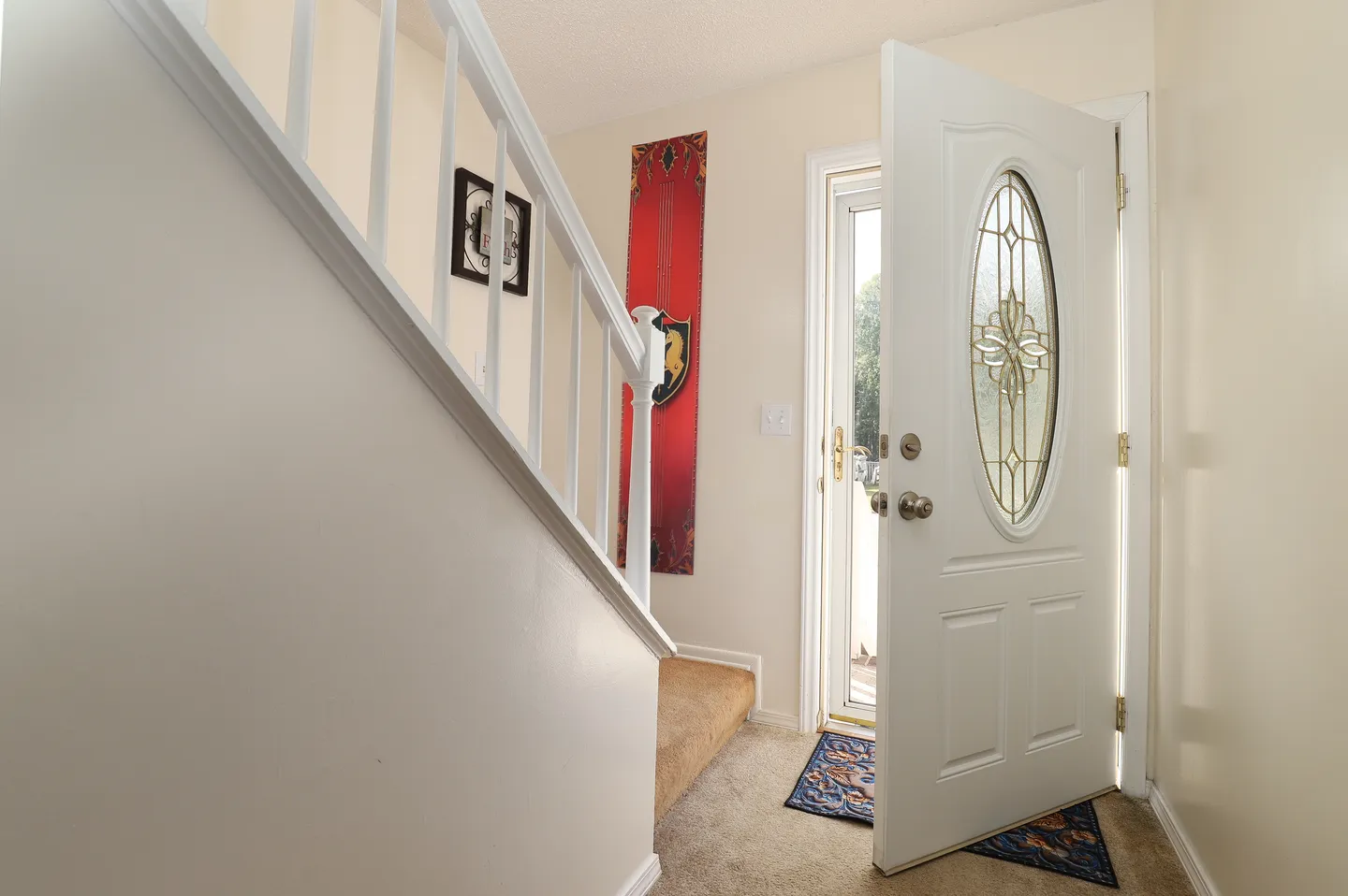 Front entryway with an open white front door, carpeted floors, and a white staircase railing.