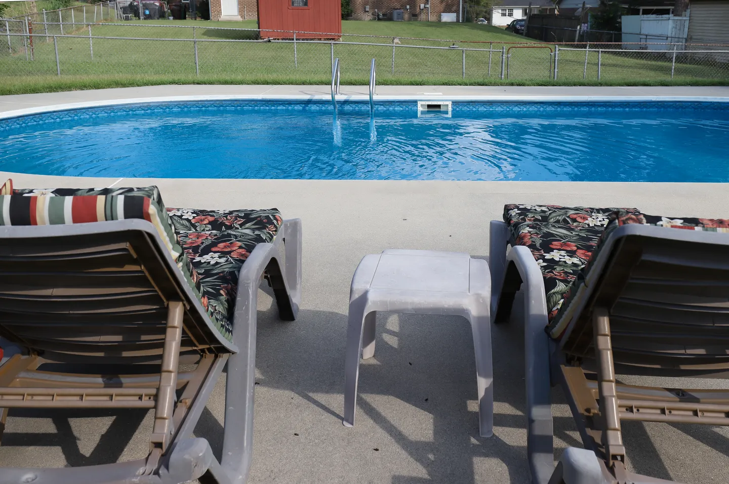 Two lounge chairs with patterned cushions beside a concrete pool deck and in-ground swimming pool.