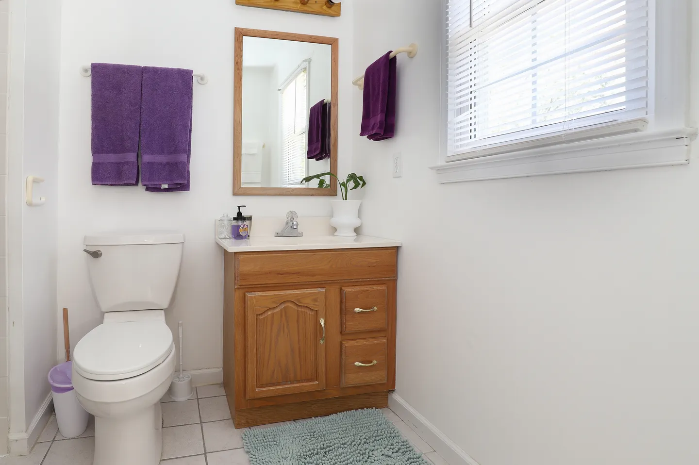 Bathroom with white toilet, wooden vanity, framed mirror, and purple towels hanging on the walls.