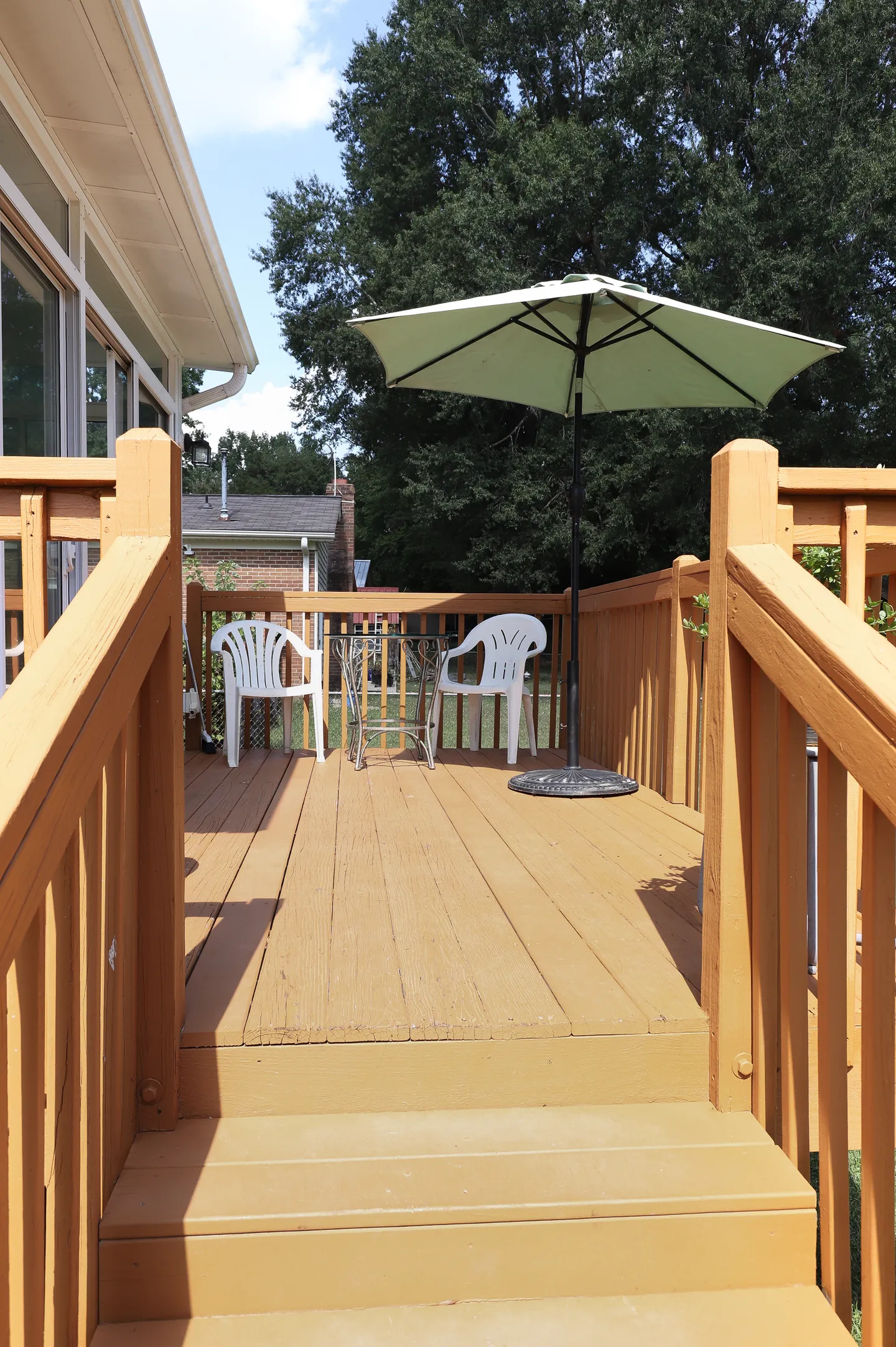 Steps leading up to an elevated wooden deck with two white chairs, a small table, and a patio umbrella.