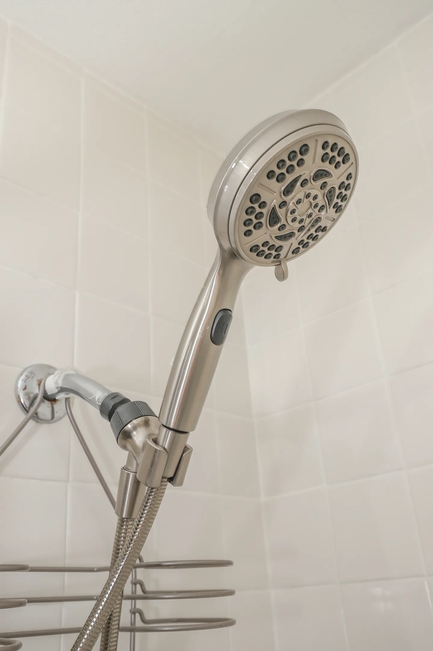 Close-up of a handheld showerhead mounted on a wall with white square tiles.