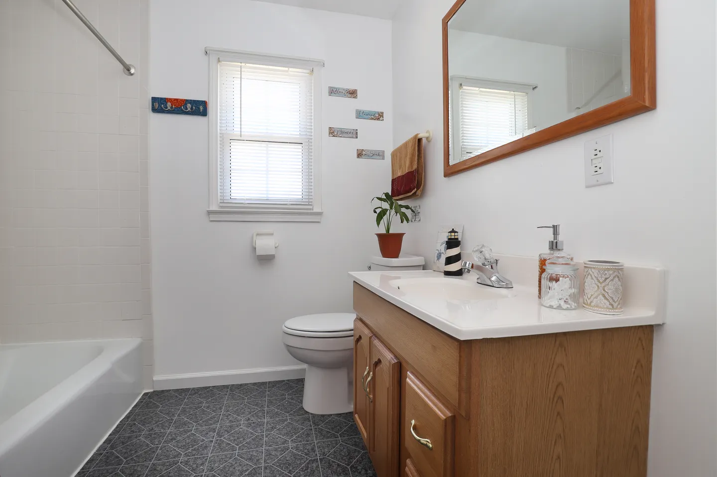 Bathroom featuring a wood vanity with a white countertop, mirror, toilet, and a white tiled bathtub.