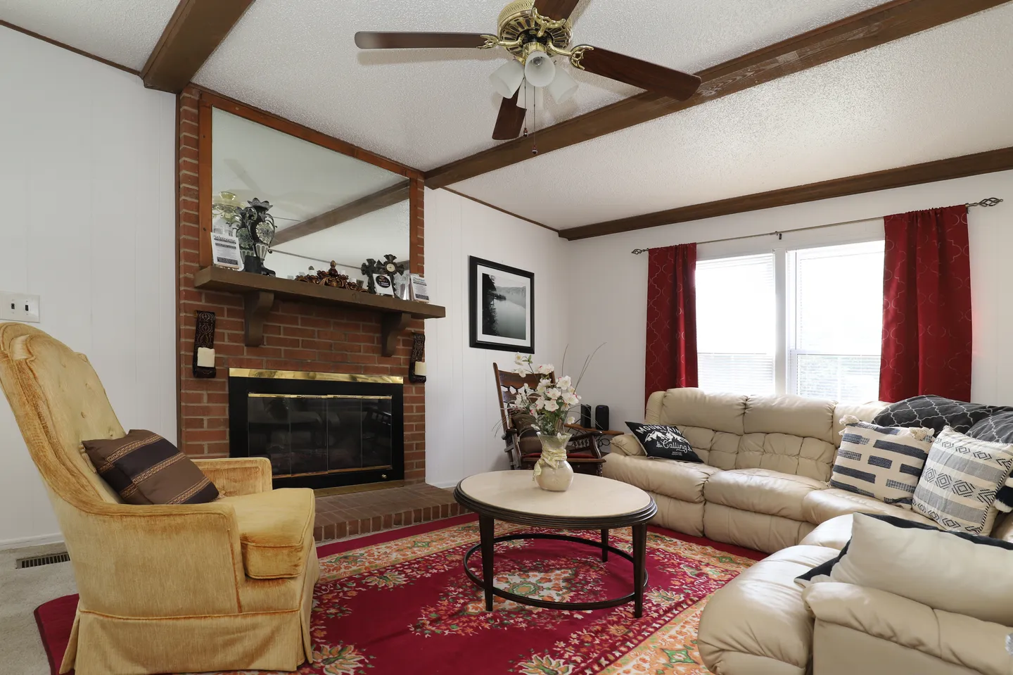 Living room with a brick fireplace, leather sectional sofa, yellow armchair, and red area rug.